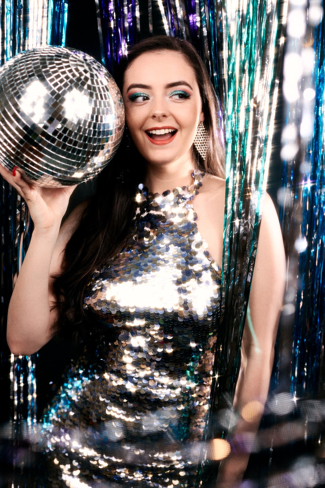 Abbey Williams stands holding a disco ball in a silver sequin dress dancing to ABBA