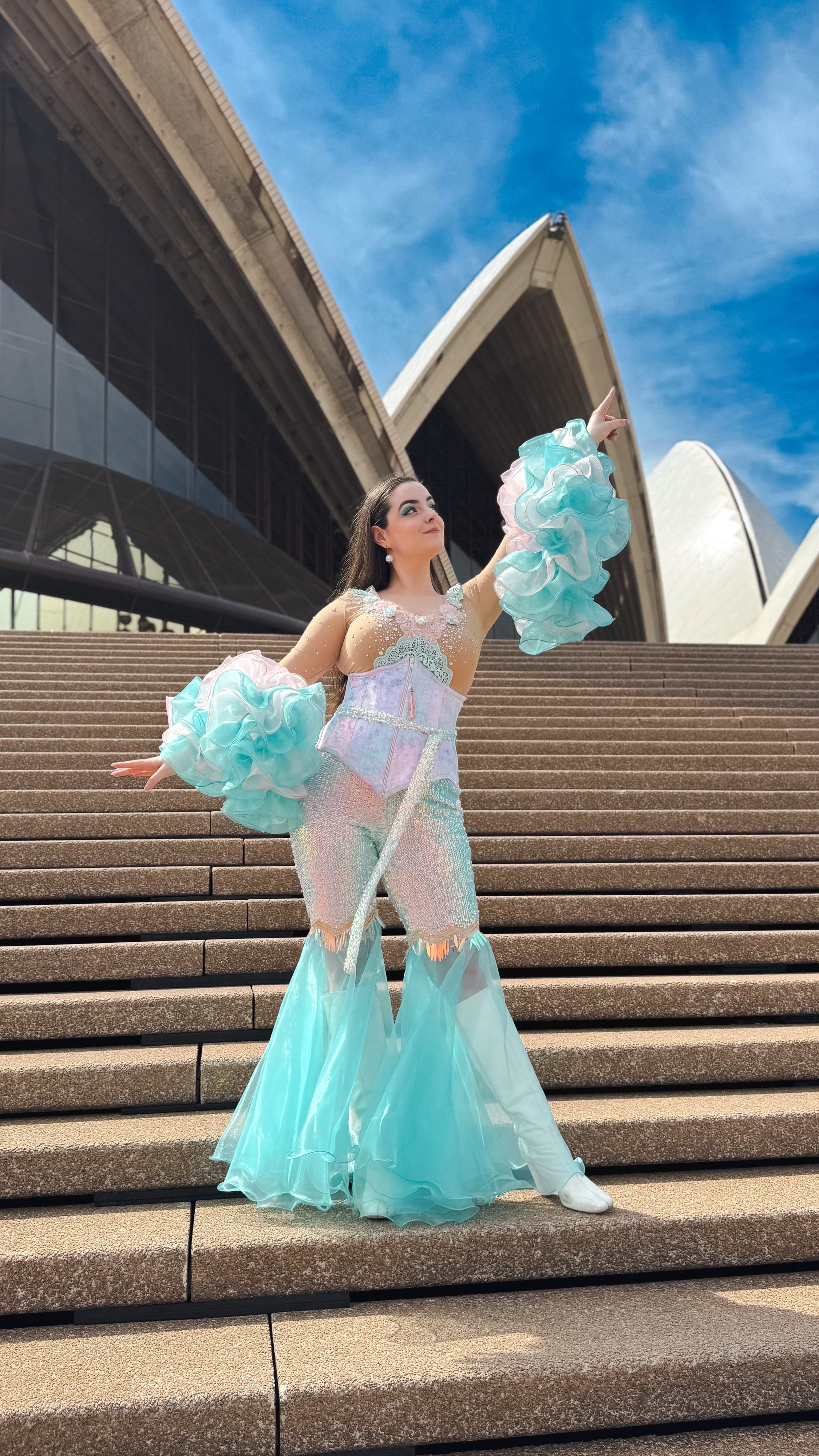 Abbey with arms outstretched in her ruffled costume in front of the Sydney Opera House sails