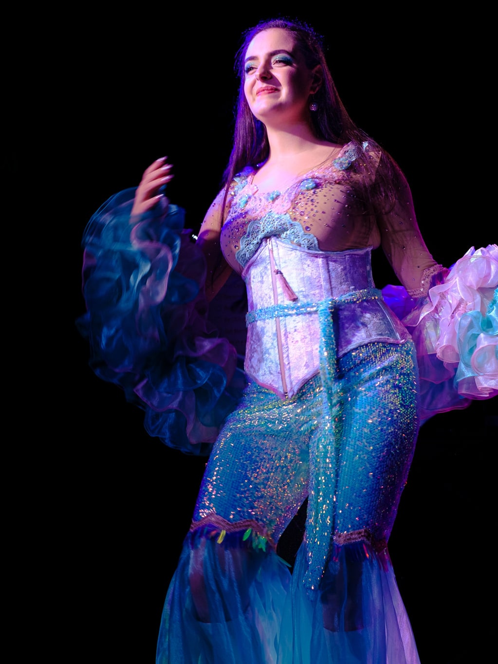 Abbey on stage in a sparkling corset and ruffled sleeves under purple light