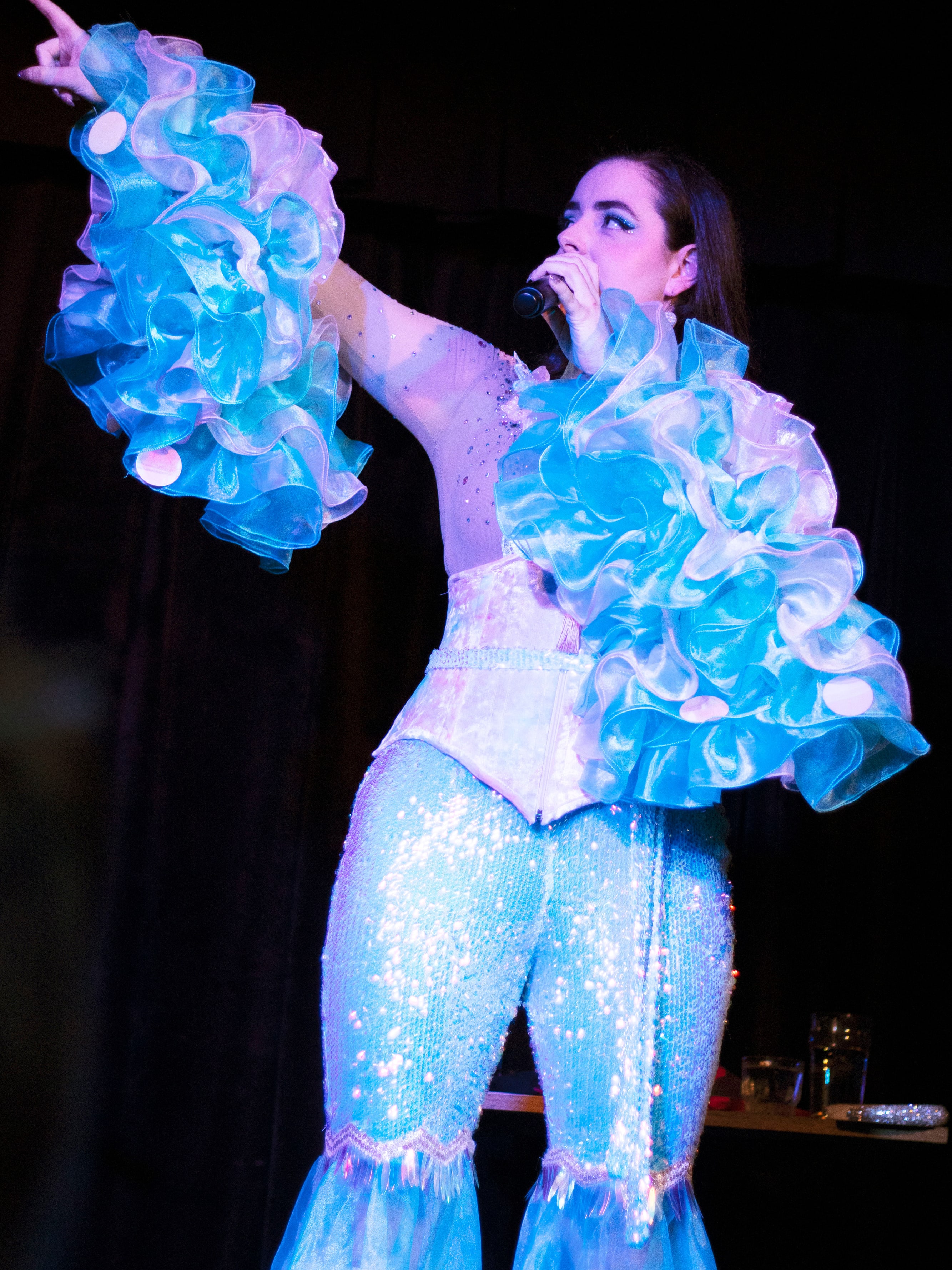 Abbey pointing to the audience mid-song in sequinned flares and ruffled sleeves