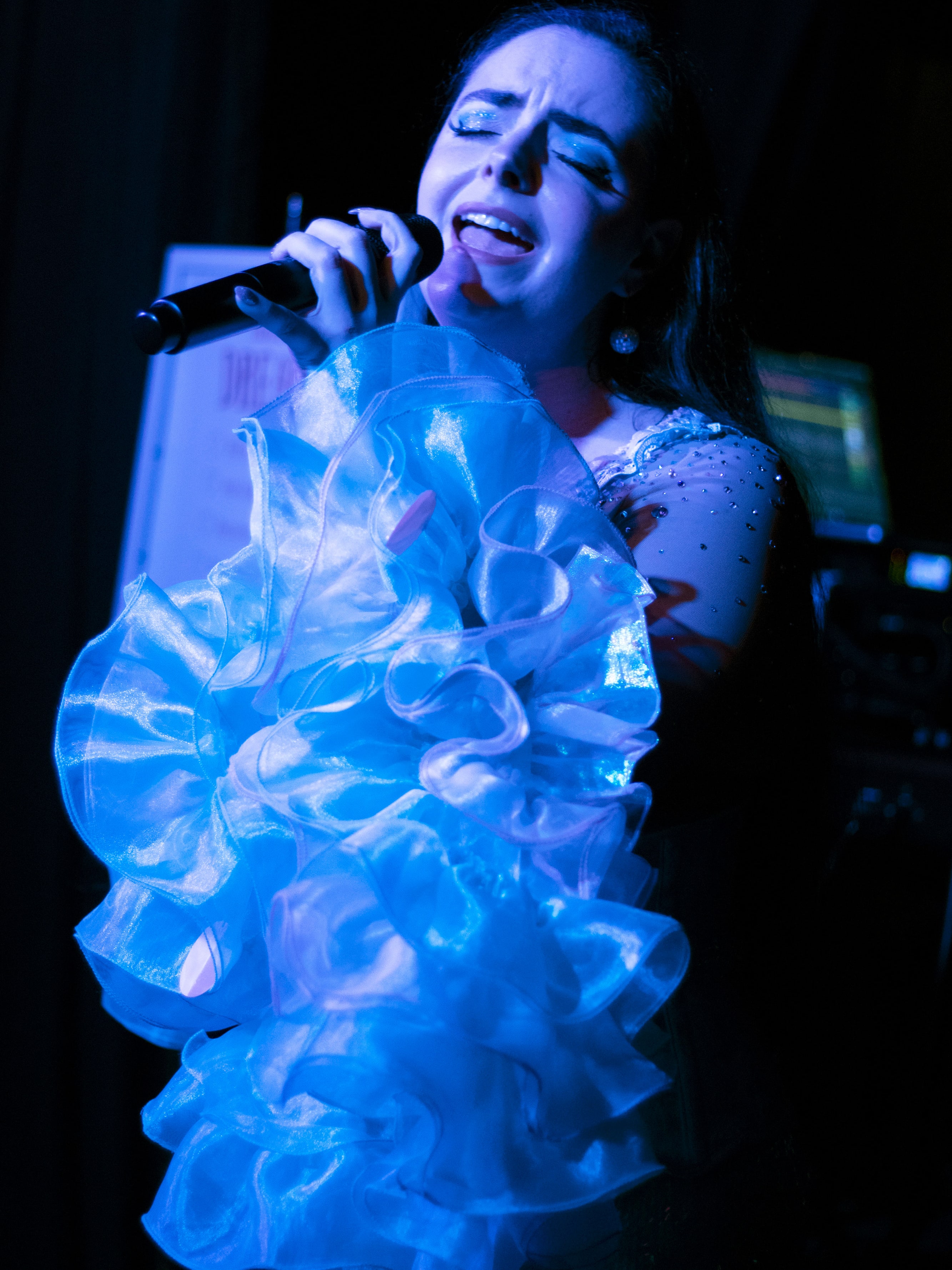 Abbey singing passionately with her eyes closed under blue light