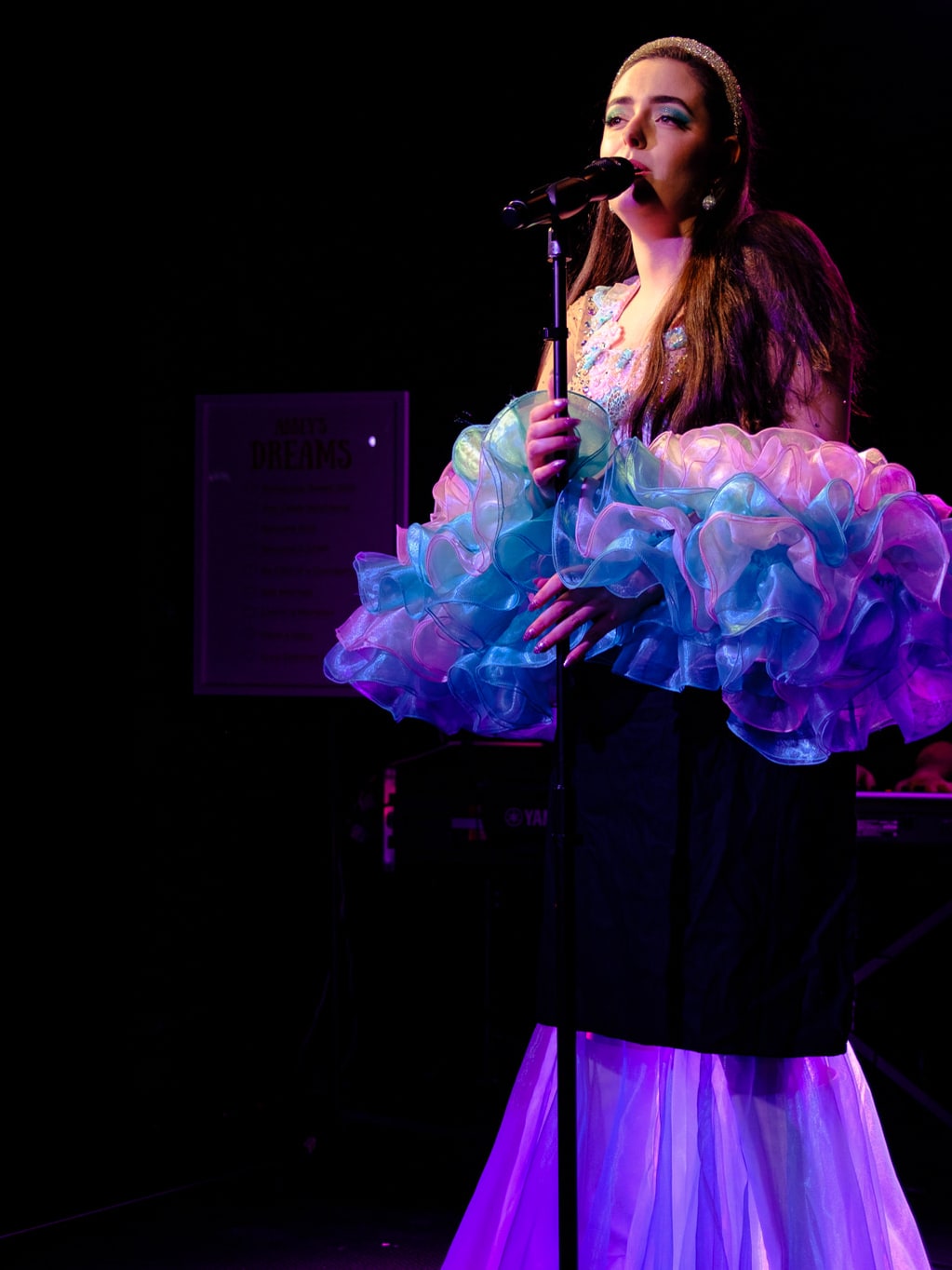 Abbey singing at a microphone stand in a spotlight