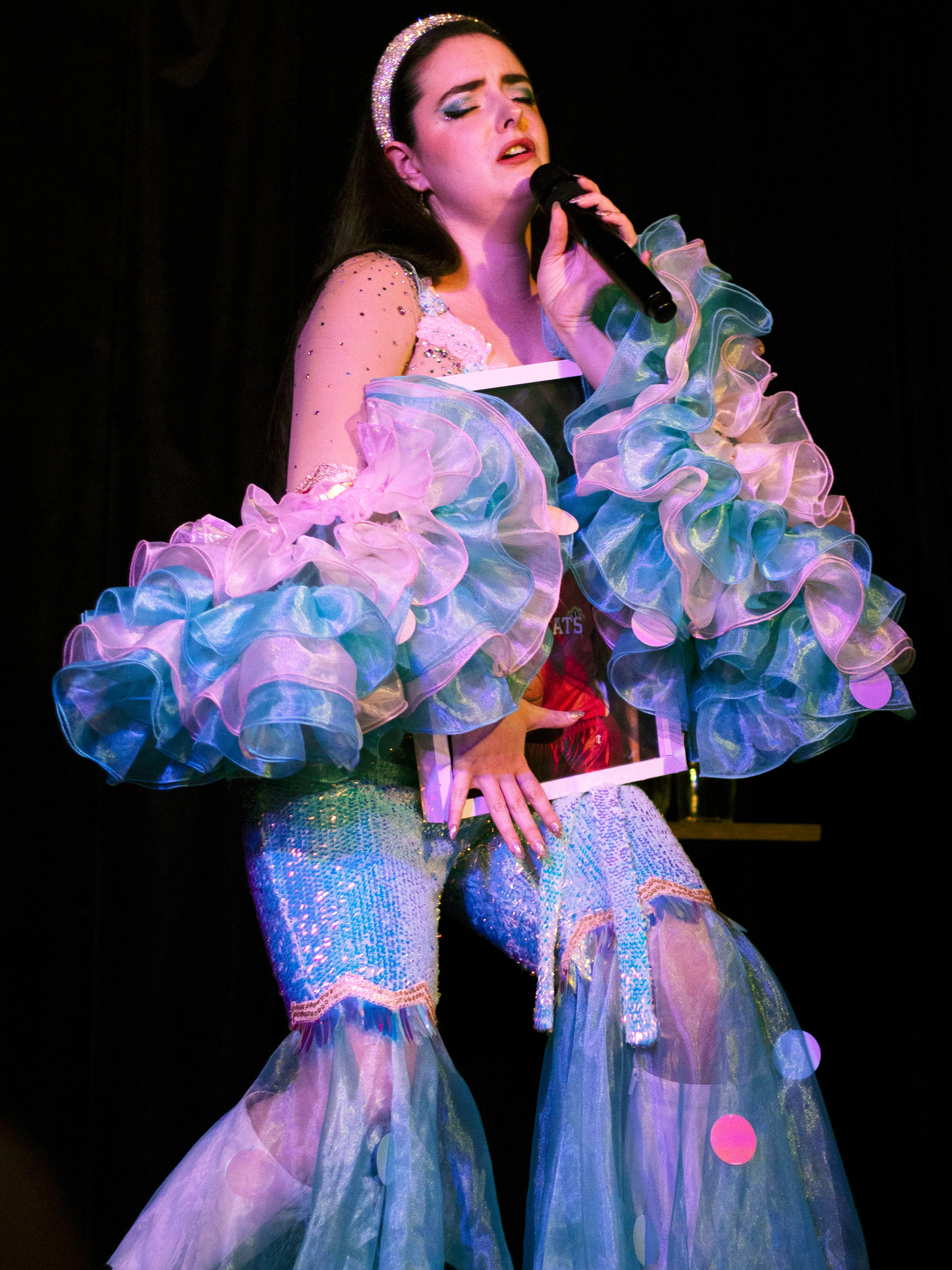 Abbey singing with a sheet of paper in hand, wearing a jewelled headband