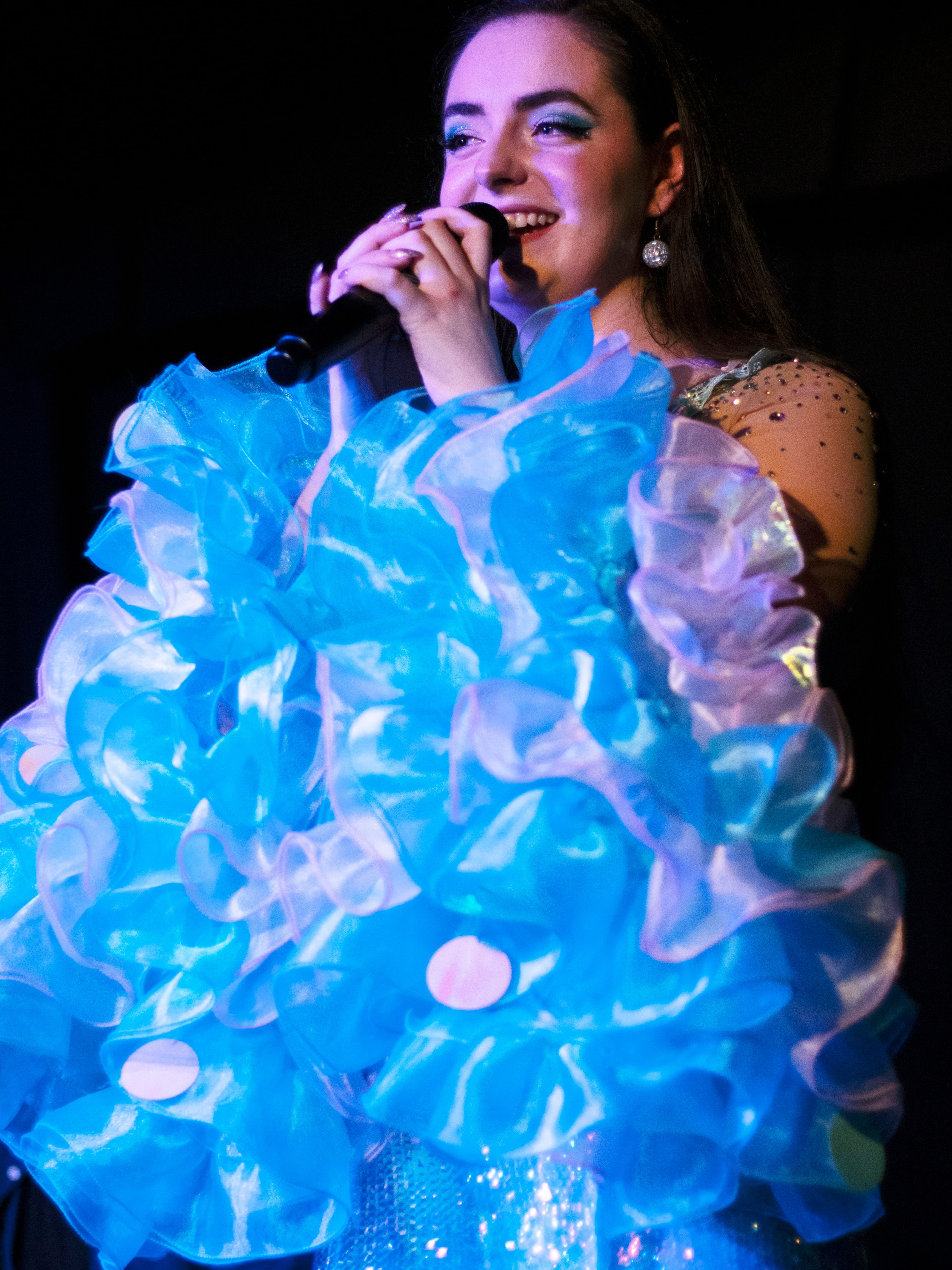 Abbey smiling at the microphone, wrapped in blue and white ruffles