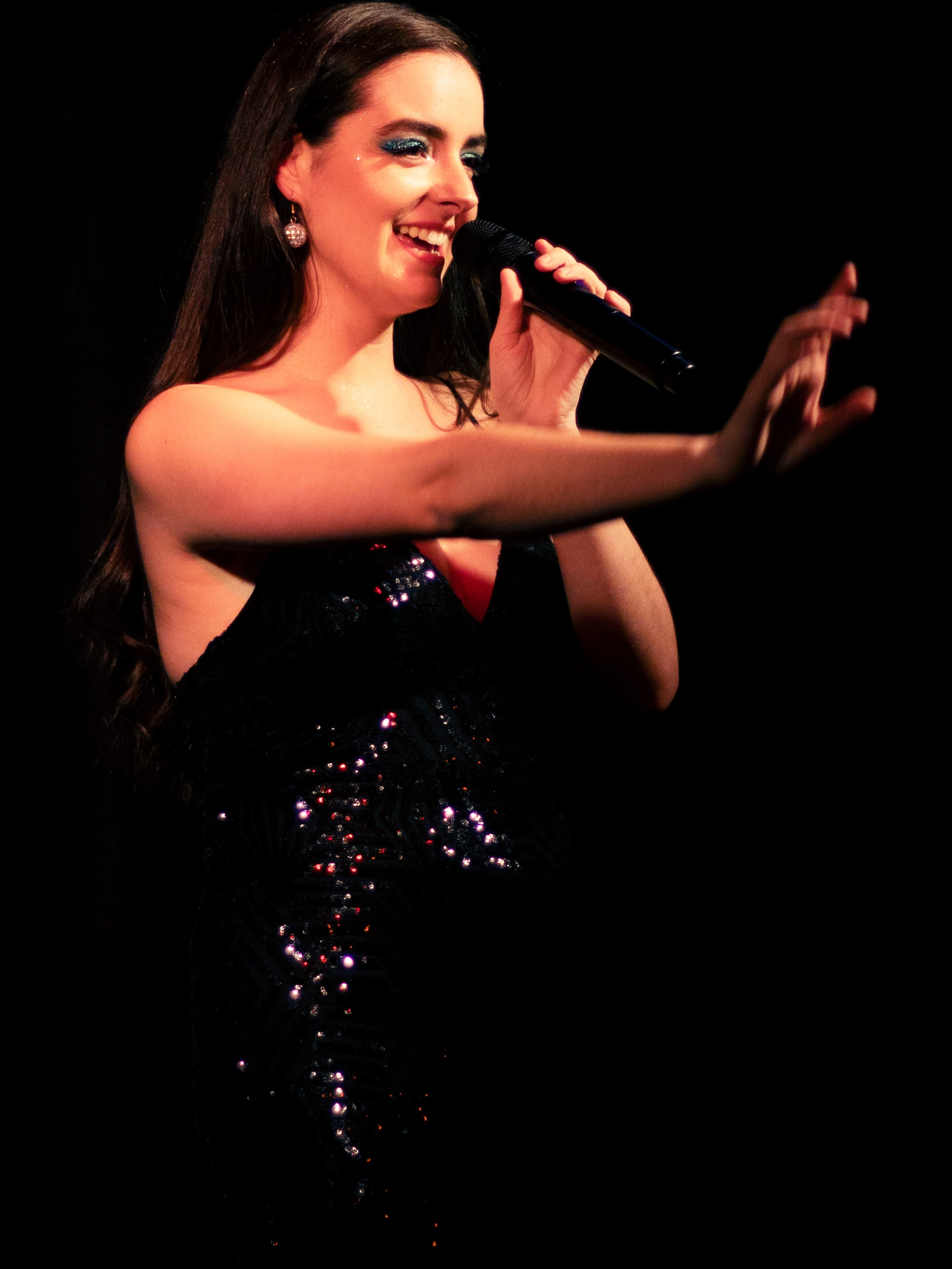 Abbey singing in a black sequin gown, one hand outstretched
