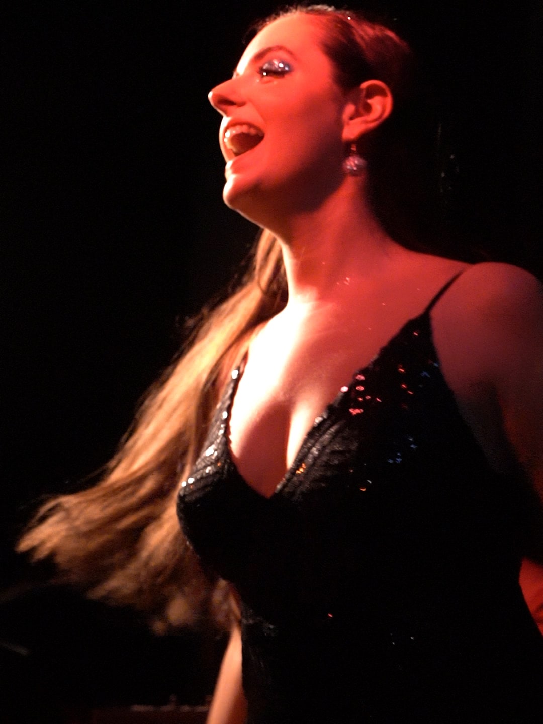 Abbey in profile under red light, singing with her head tilted back