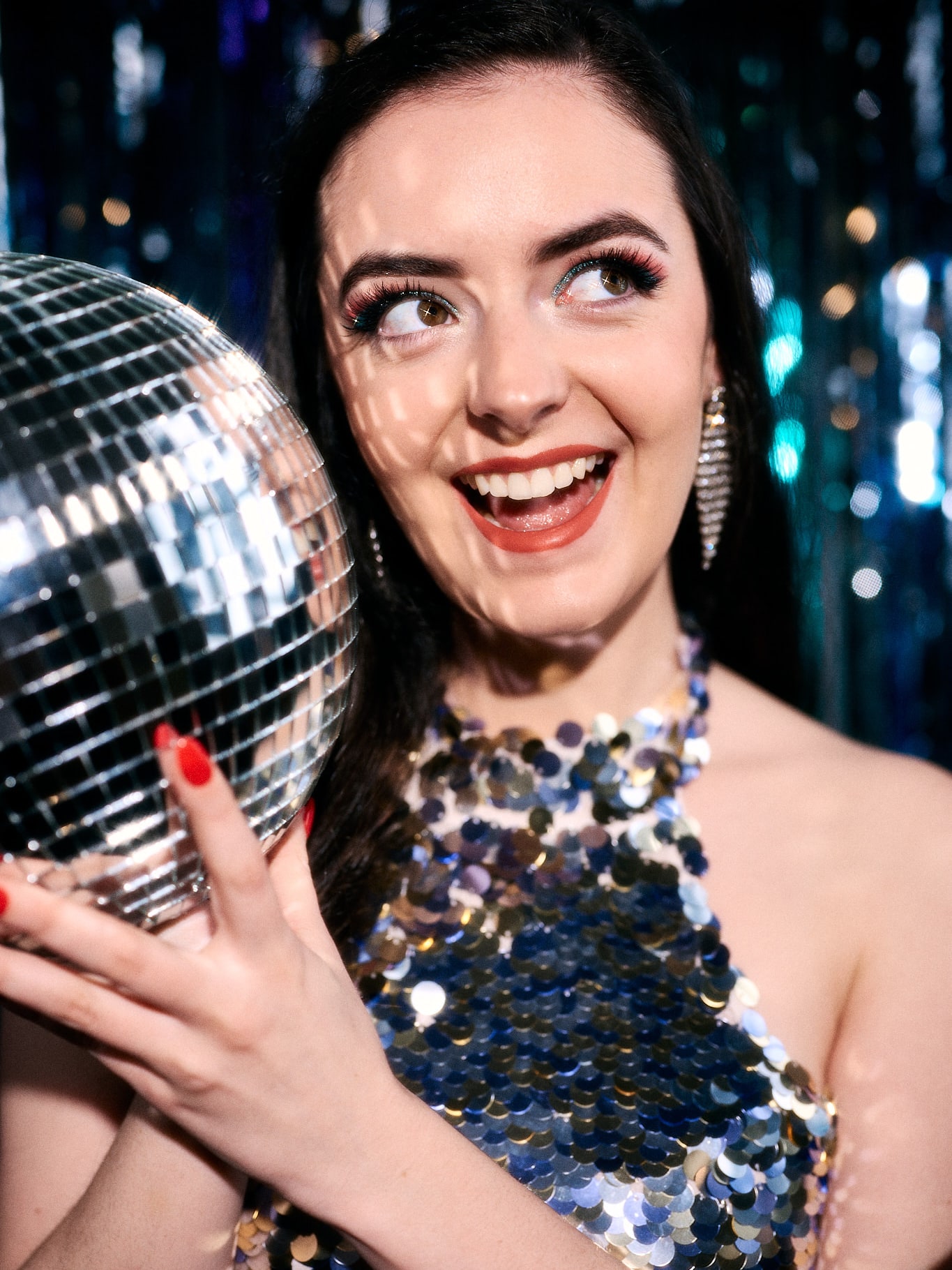 Abbey laughing and holding a disco ball in a sequin halter dress
