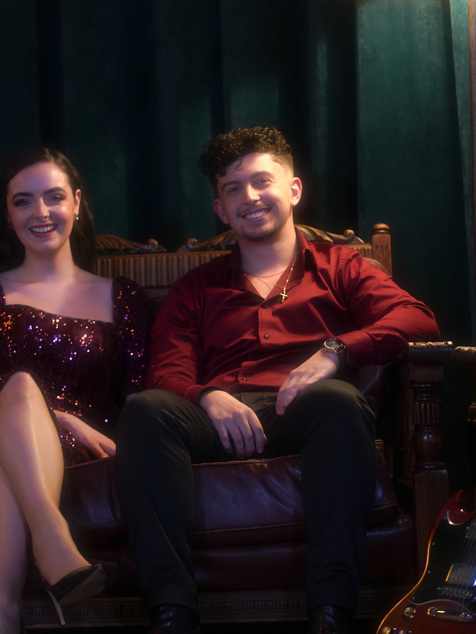 Abbey and her guitarist sitting on a leather sofa with an electric guitar resting beside them