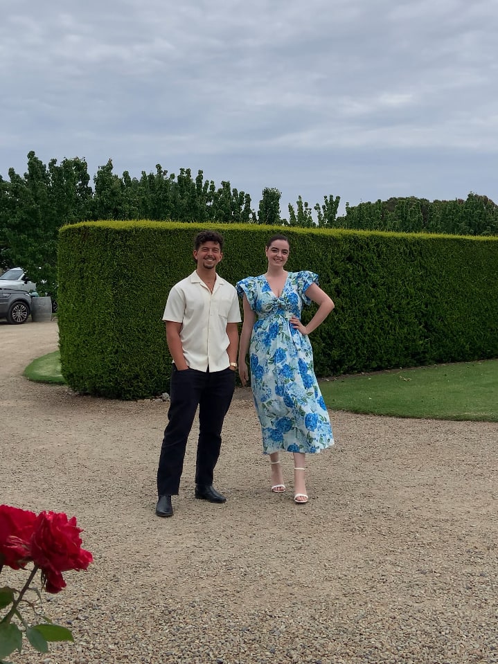 Abbey and her guitarist standing on a gravel driveway in front of a manicured hedge at a wedding venue