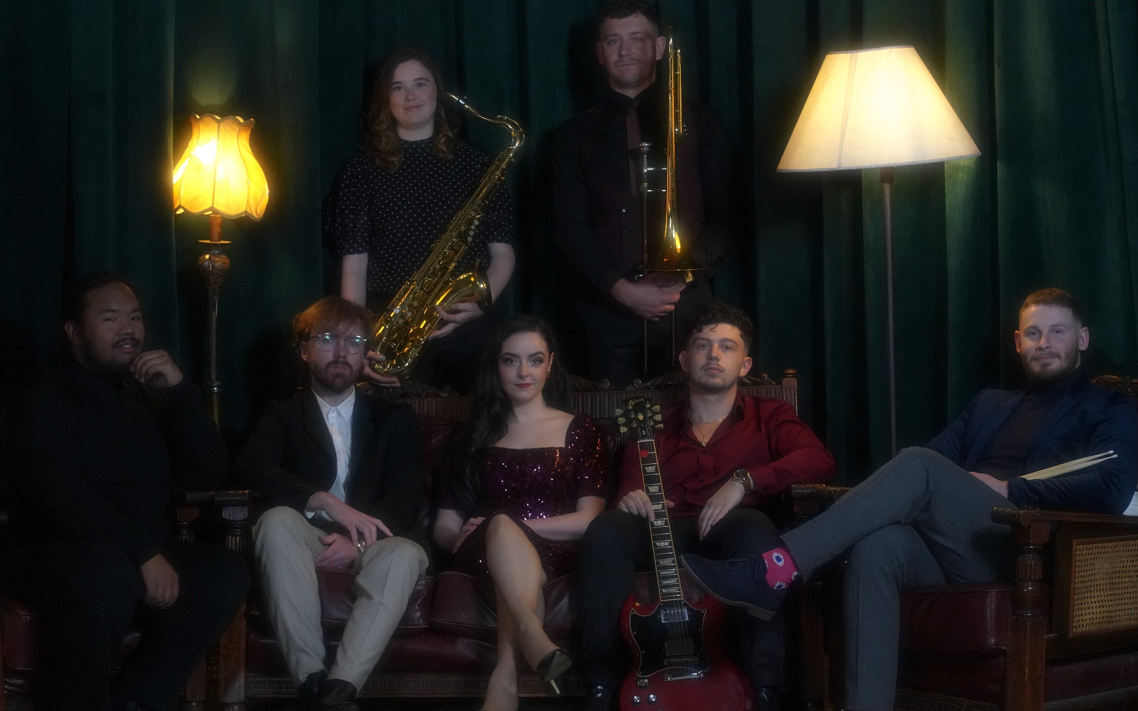 The Cherry Lane band posed around Abbey on leather armchairs in a lamp-lit lounge with green curtains