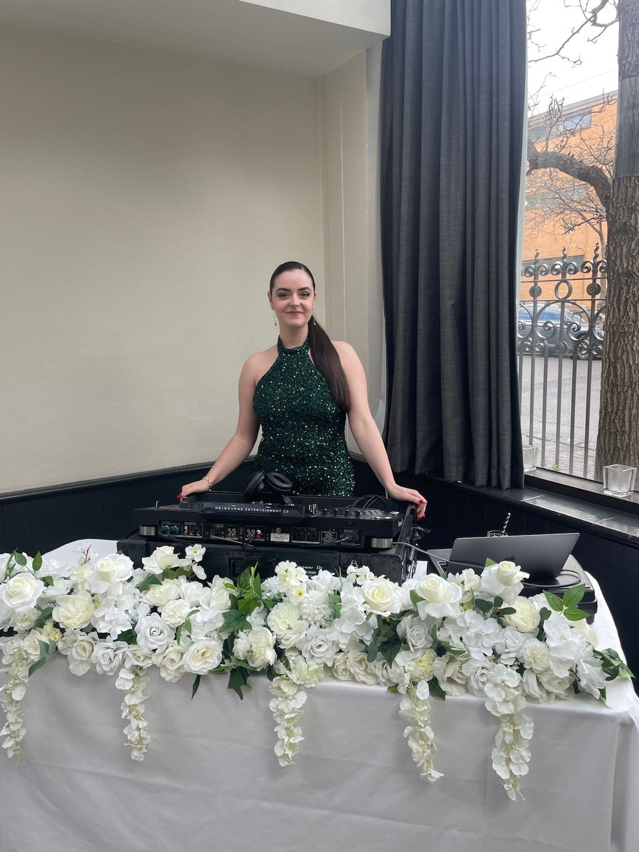 Abbey at her DJ decks on a table draped in white flowers at a wedding reception