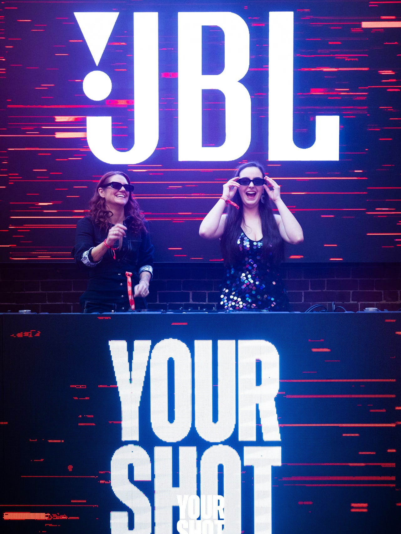 Abbey and Cass on stage beneath the JBL logo and YOURSHOT banner