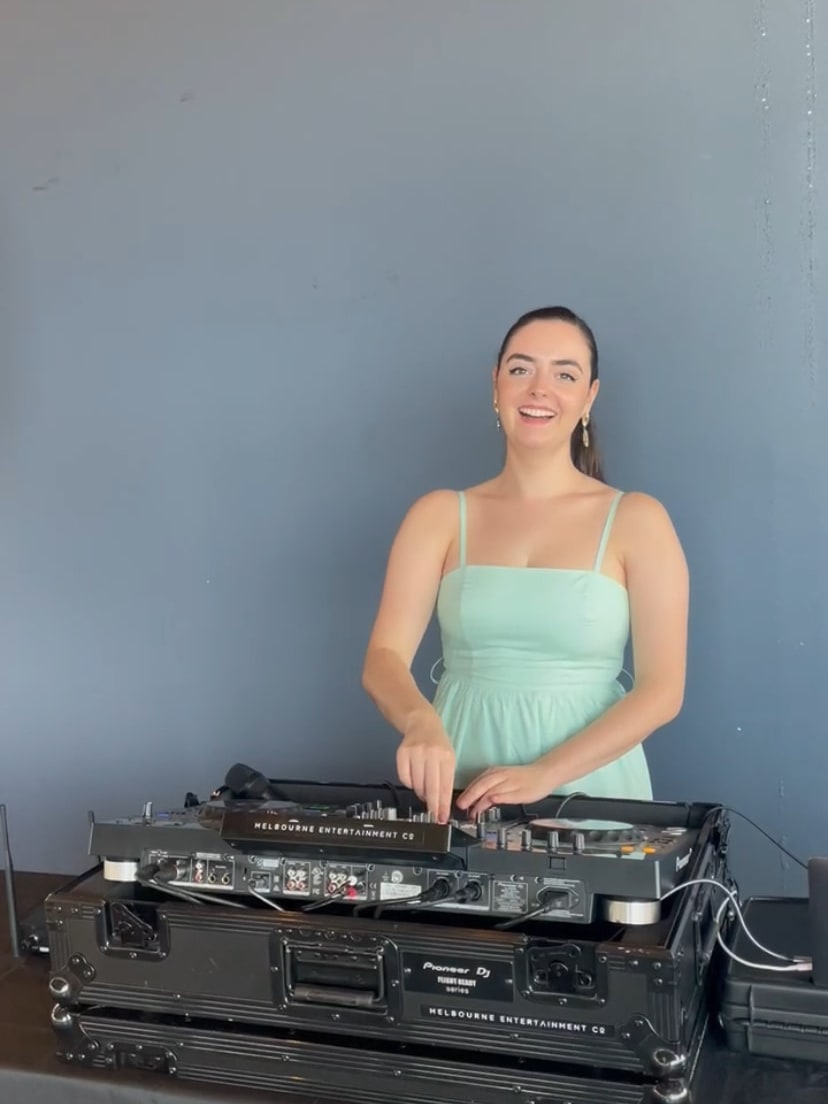 Abbey smiling behind her DJ decks in a mint green dress