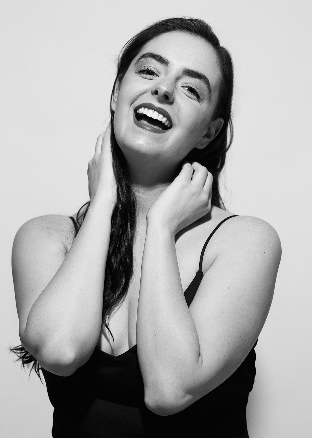 Black and white portrait of Abbey laughing with her hands at her neck