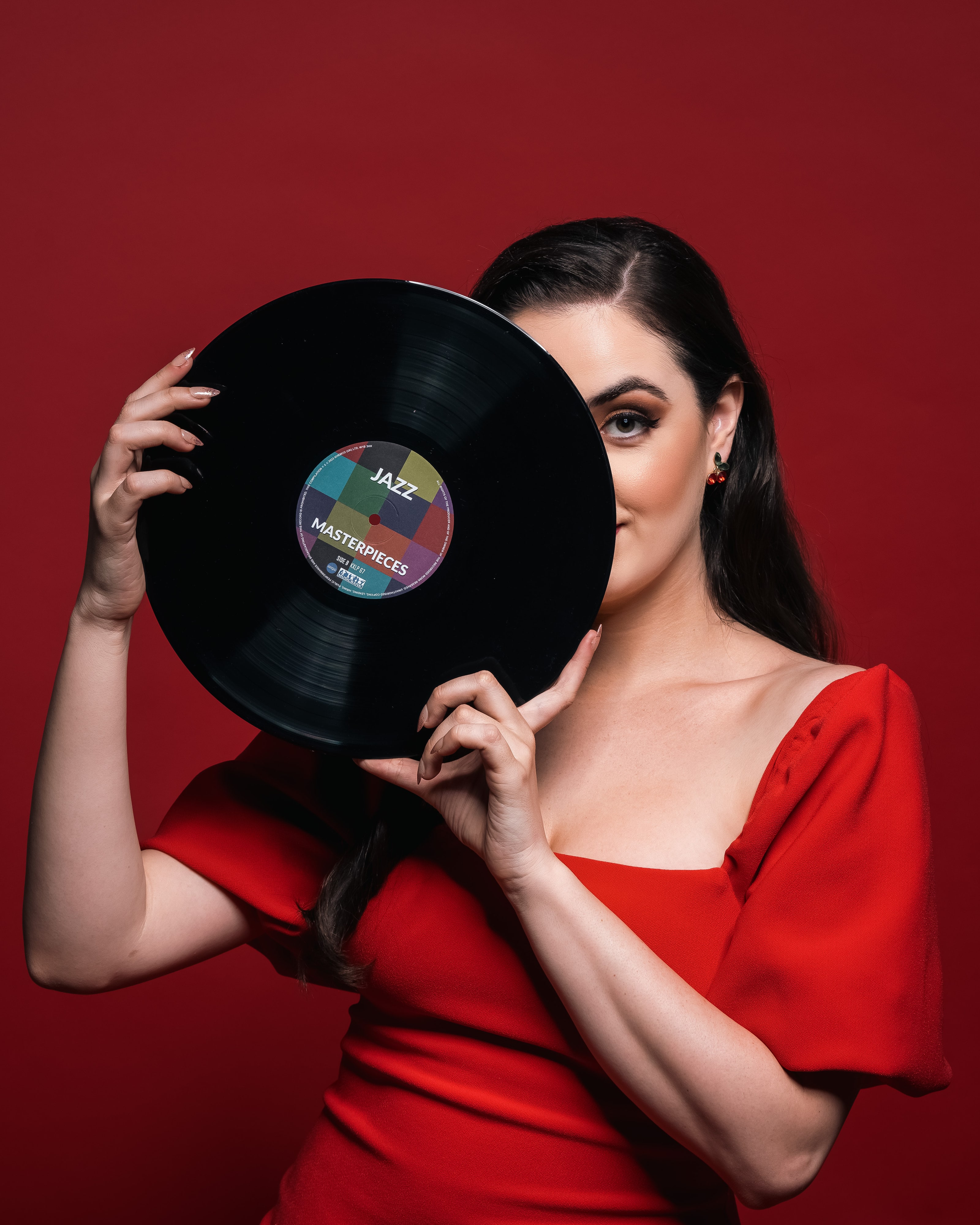 Abbey in a red dress holding a jazz vinyl record over half of her face against a red backdrop