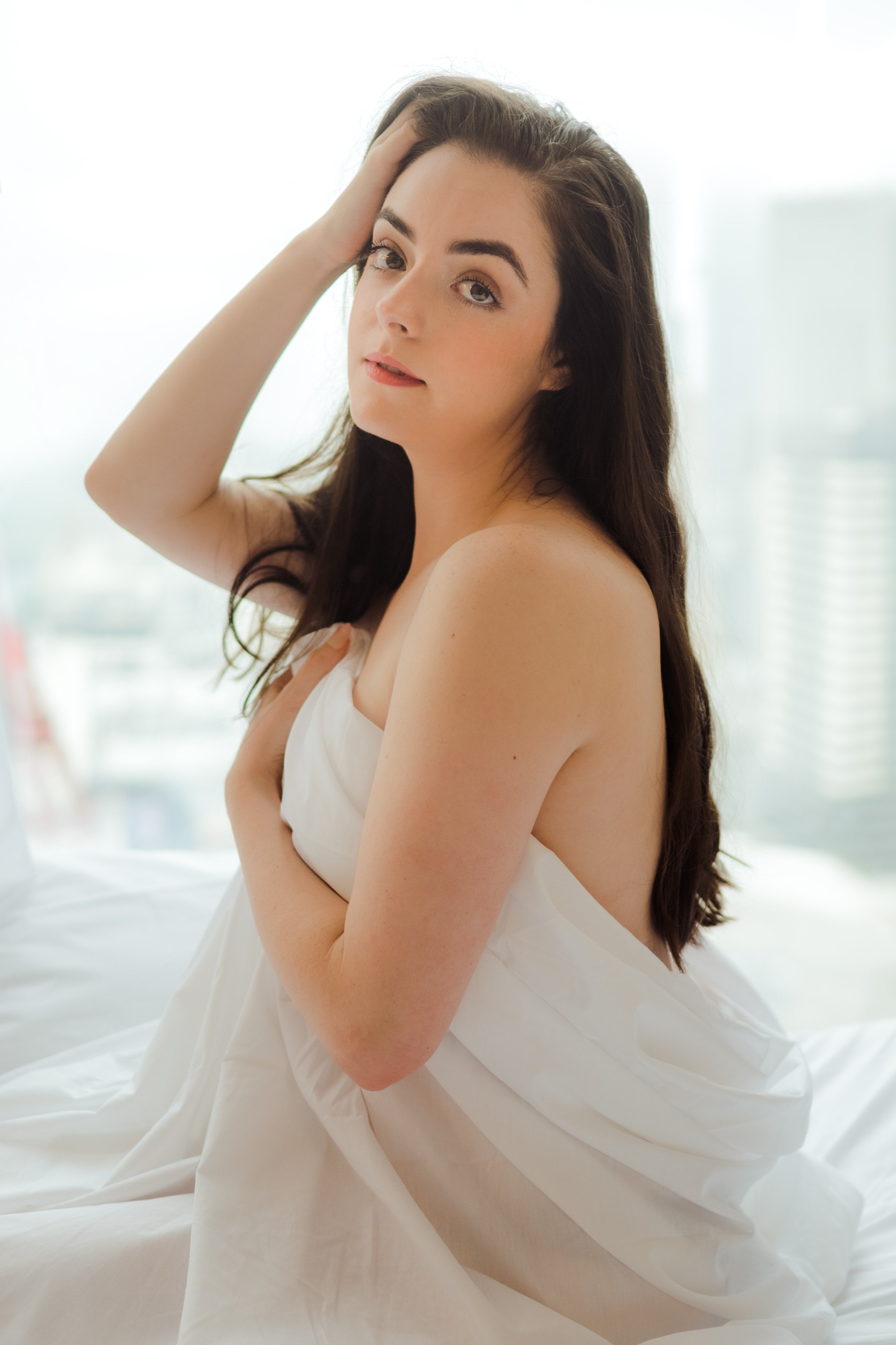 Abbey wrapped in white sheets beside a window with a city view
