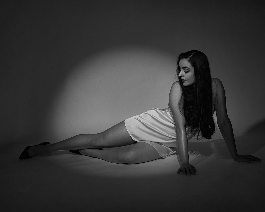 Black and white shot of Abbey lying on the floor in a pool of spotlight in a white slip dress
