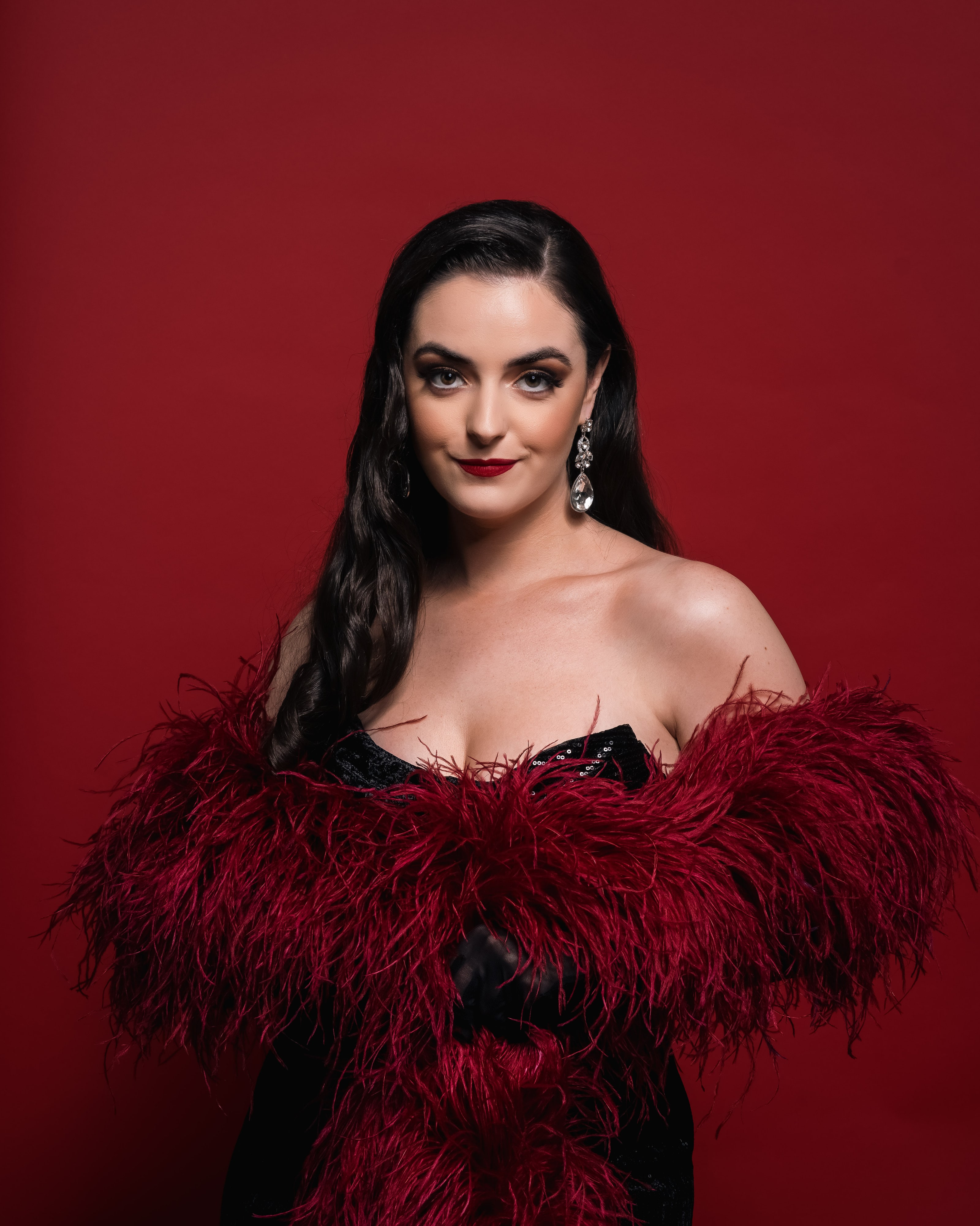 Abbey in a black dress and red feather stole against a red backdrop