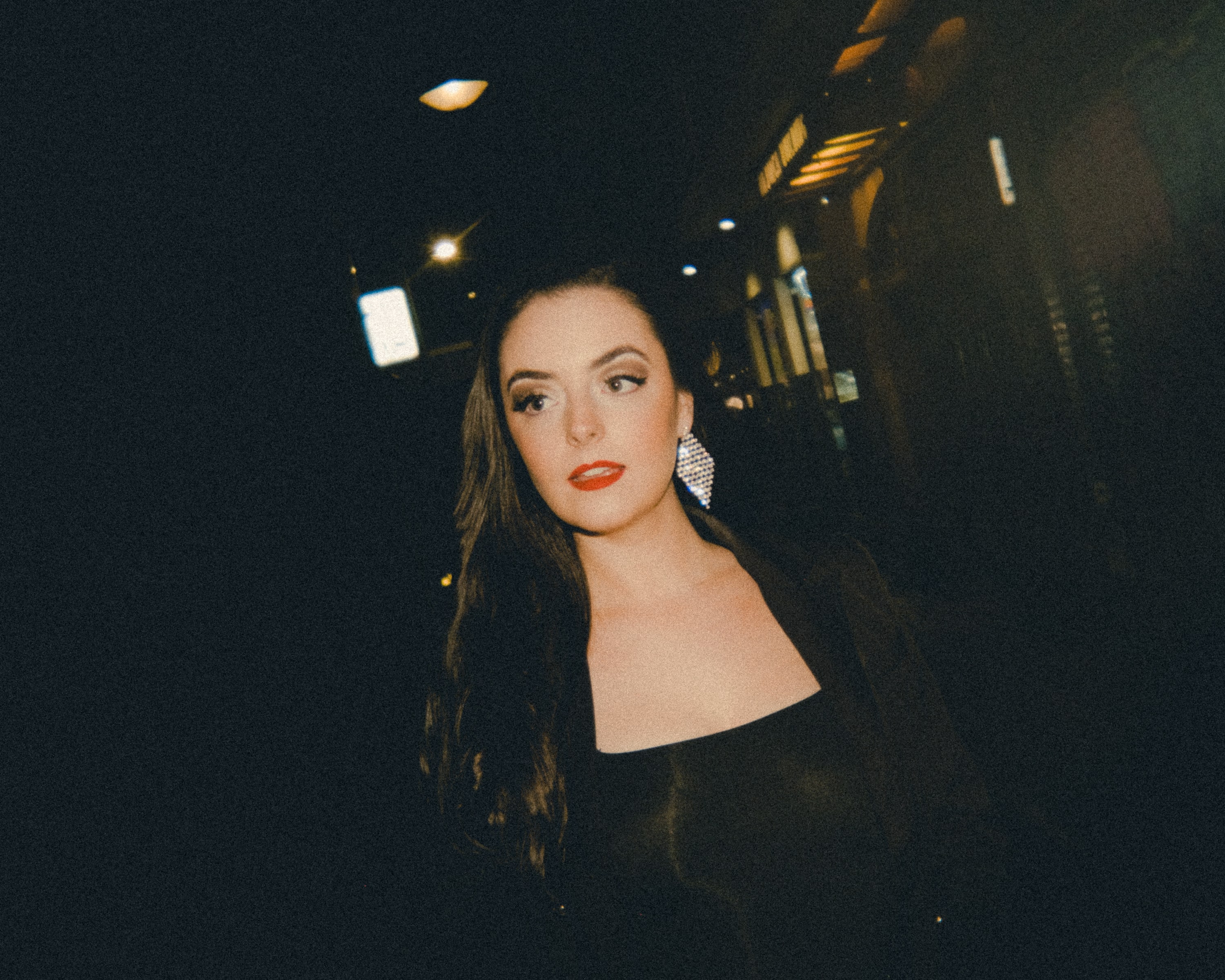 Abbey in a black dress with red lipstick in a dimly lit city laneway at night