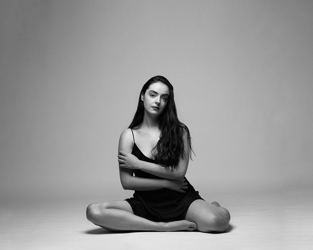 Black and white studio shot of Abbey sitting cross-legged in a black slip dress