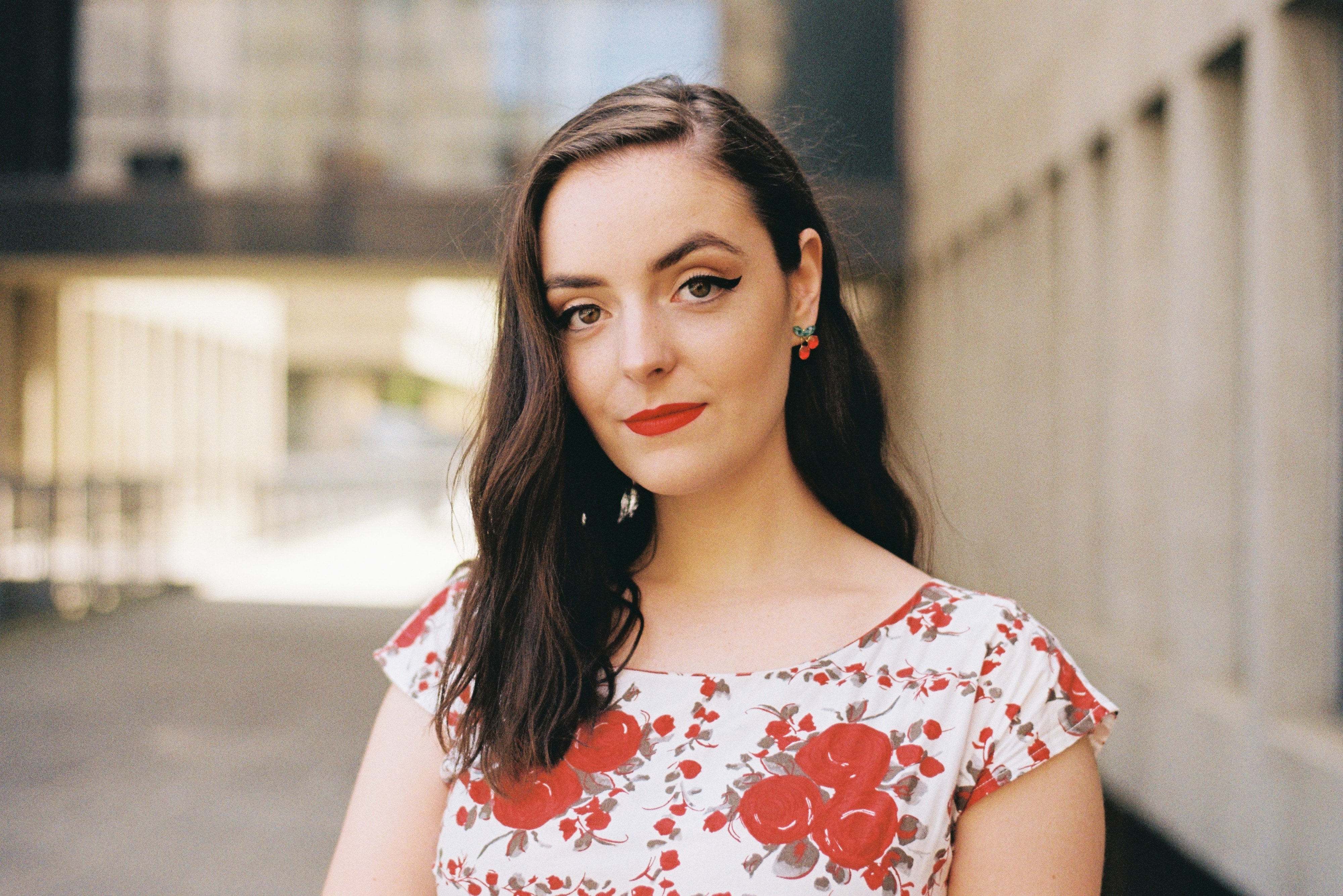 Abbey in a red and white floral top with red earrings in a city laneway