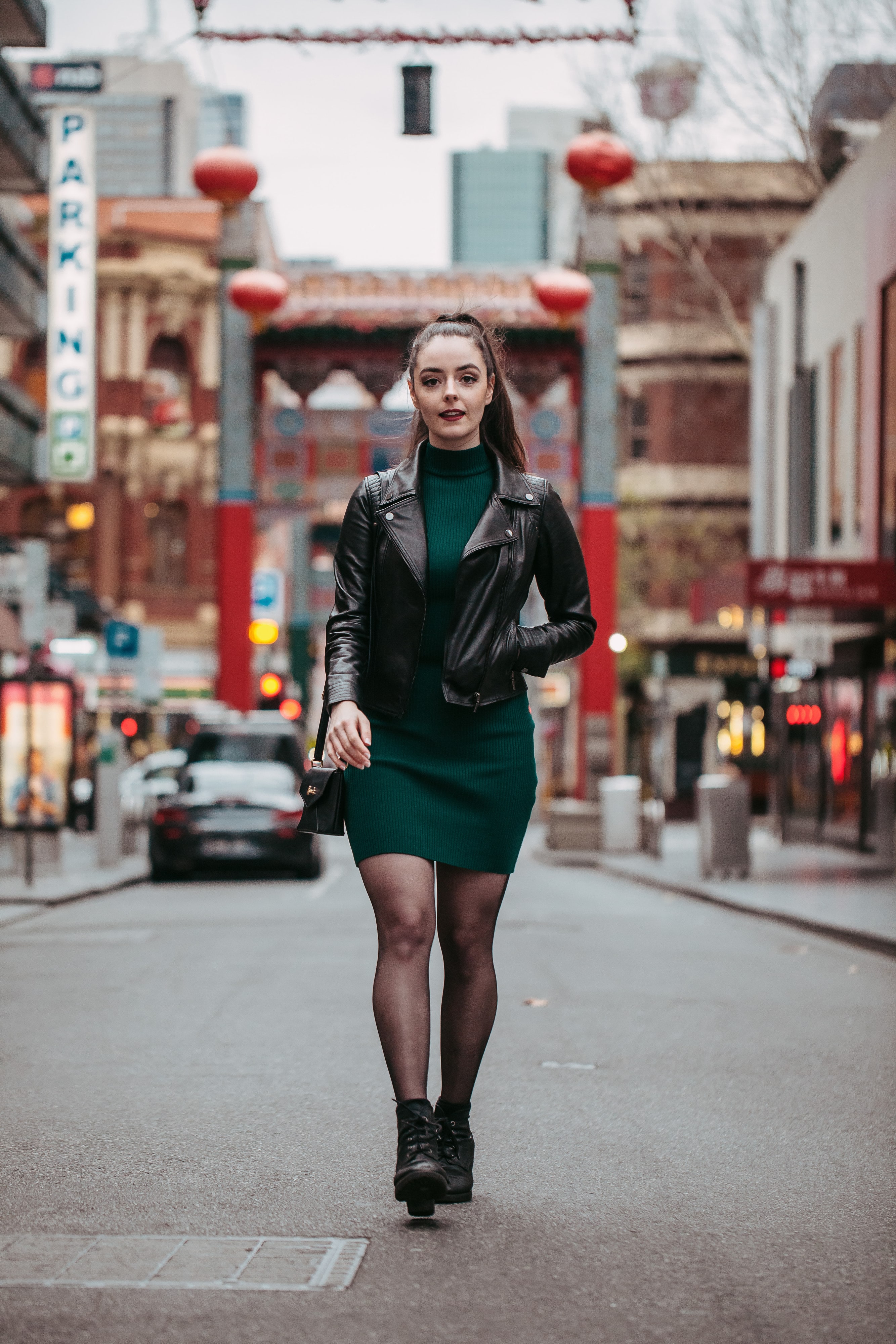 Abbey walking down a Chinatown street in a leather jacket and green dress