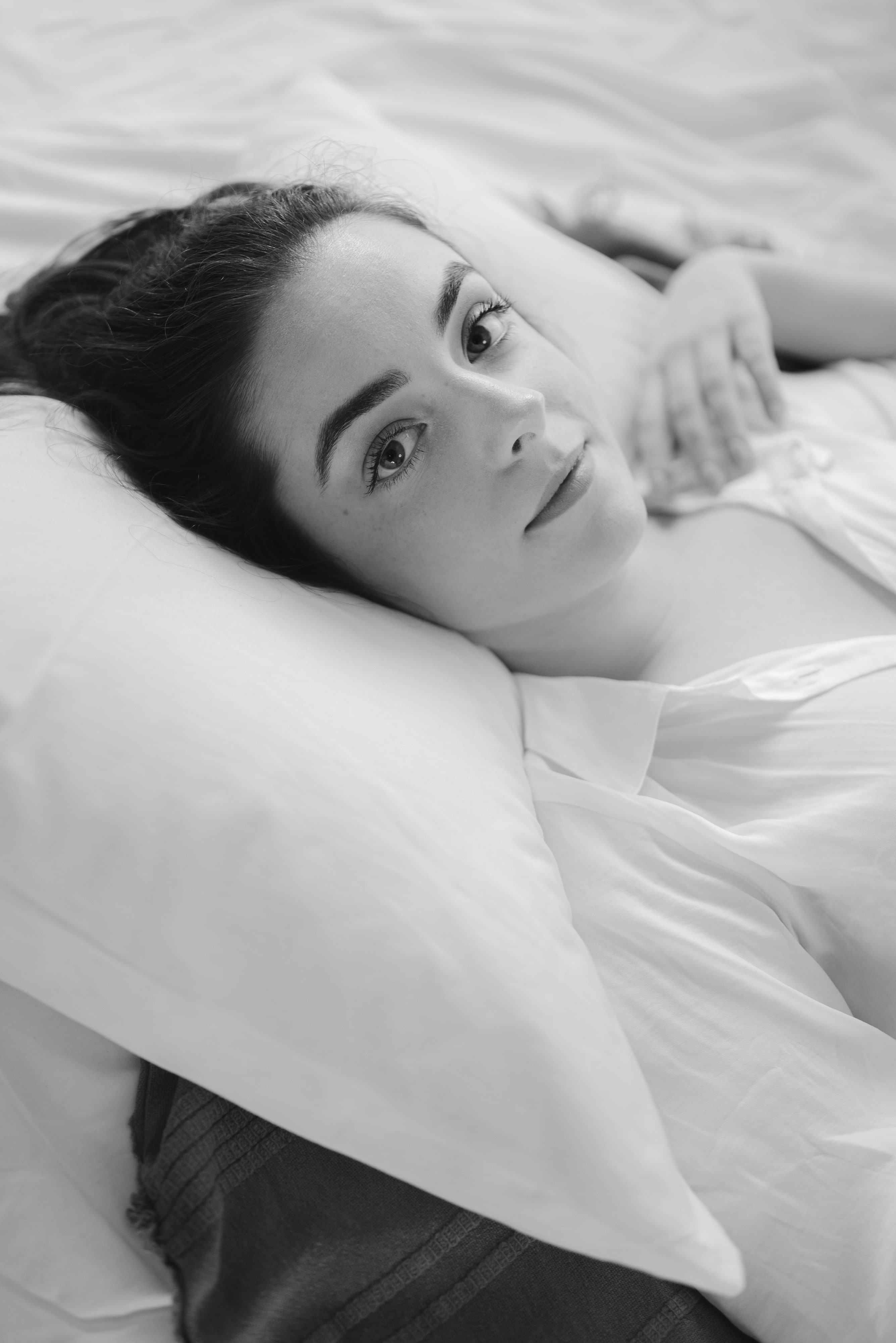 Black and white shot of Abbey lying back on white pillows