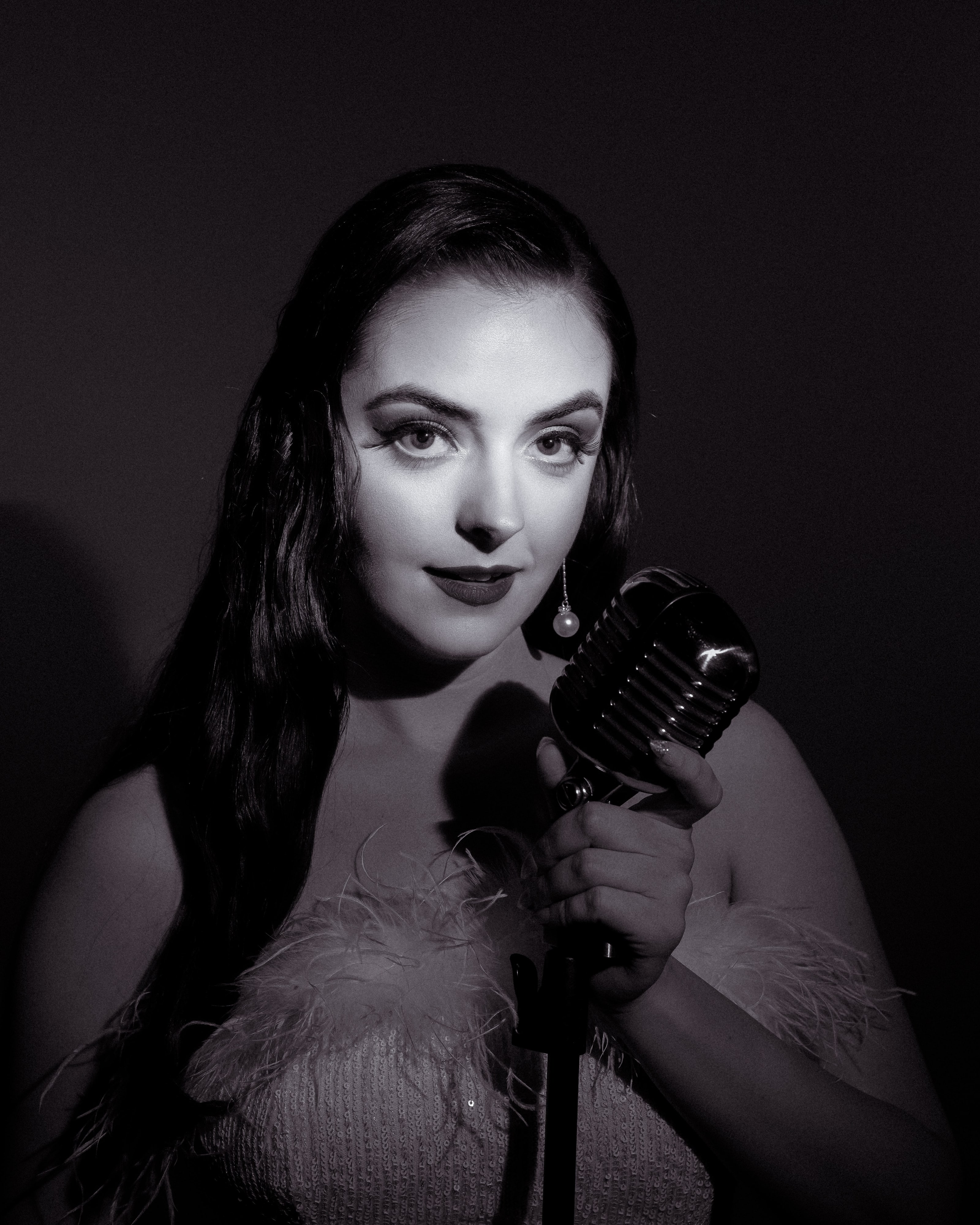 Black and white portrait of Abbey at a vintage microphone in a feathered gown