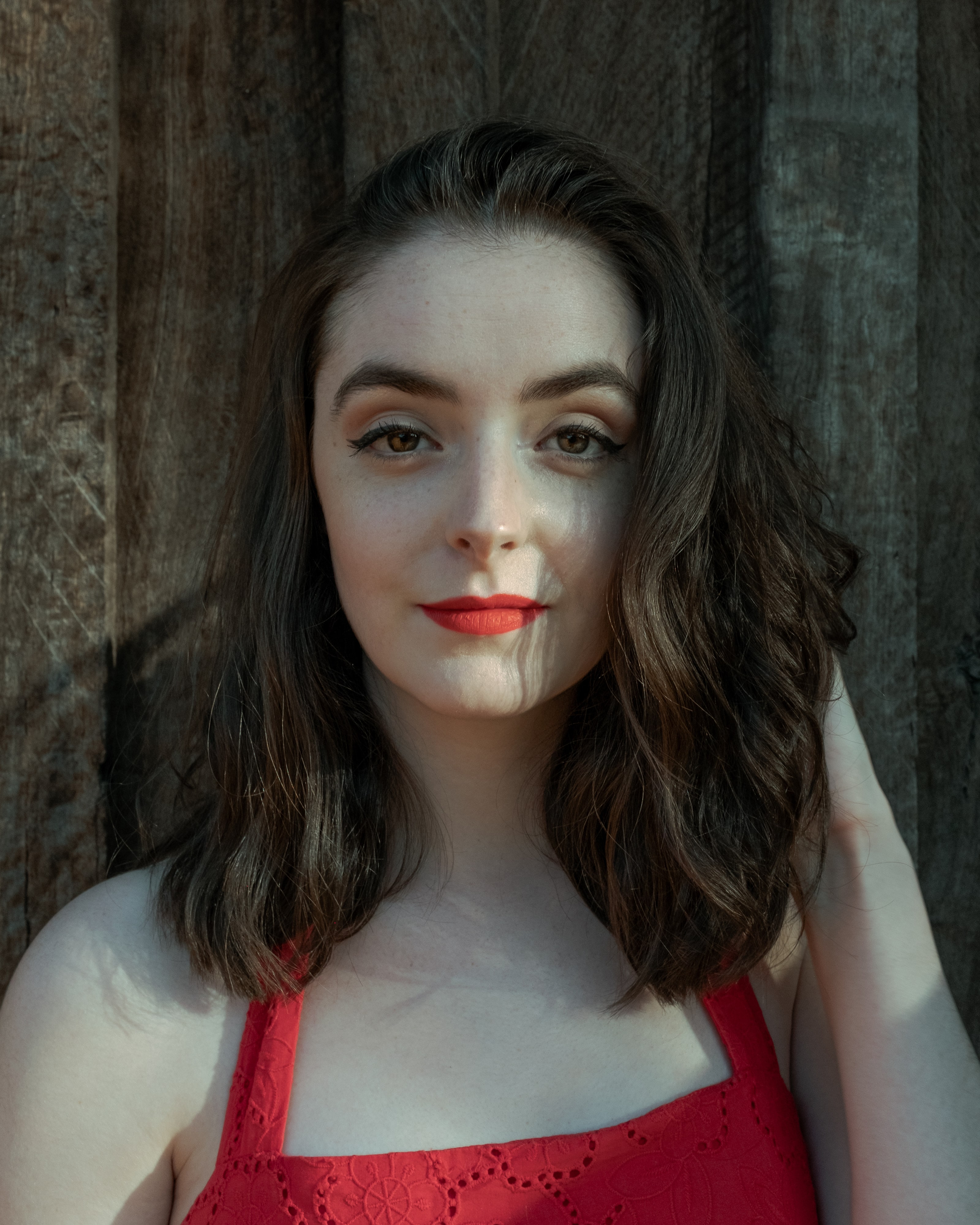 Abbey with shoulder-length wavy hair in a red top, light falling across her face