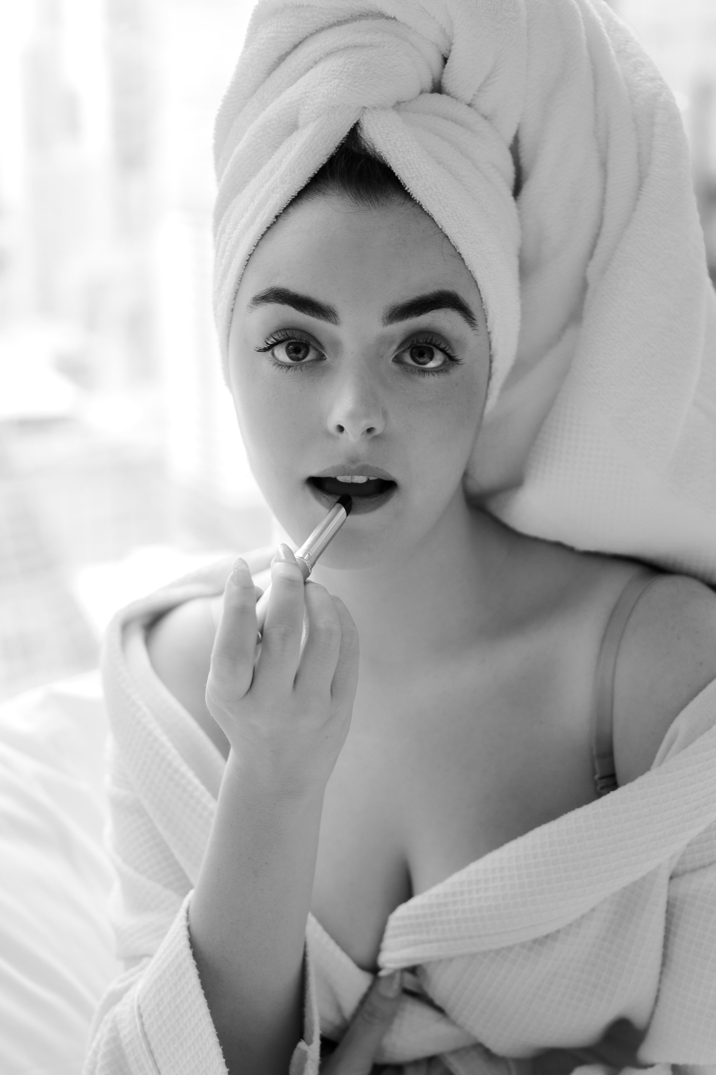 Black and white shot of Abbey in a towel turban and robe applying lipstick