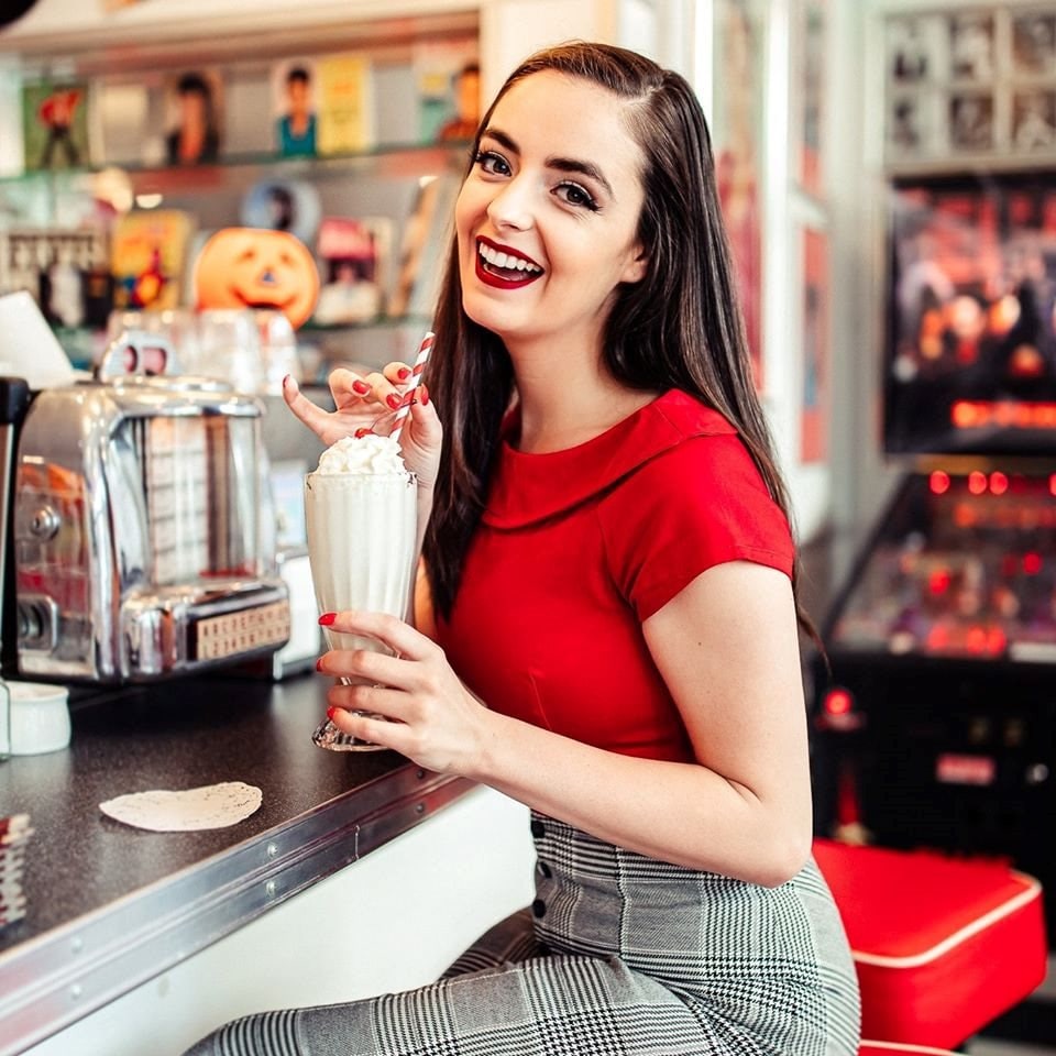 Abbey in a red top holding a milkshake at a retro diner counter