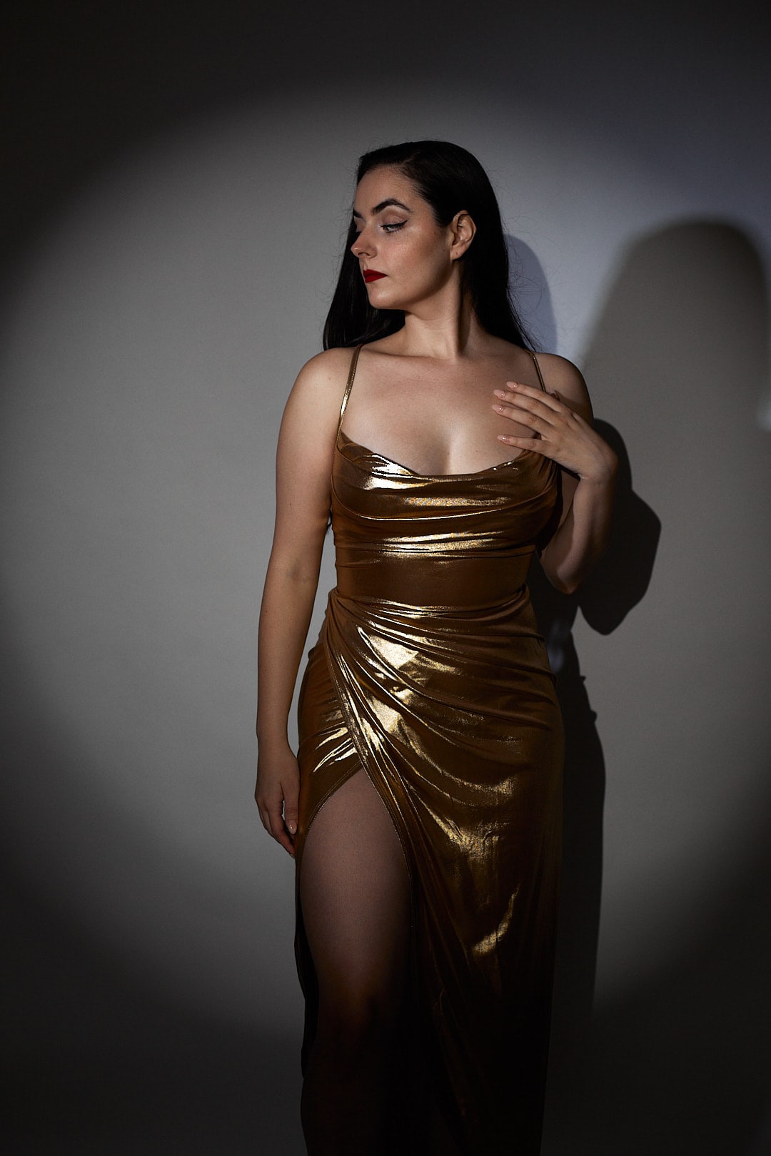 Abbey in a draped gold satin gown standing in a circle of spotlight