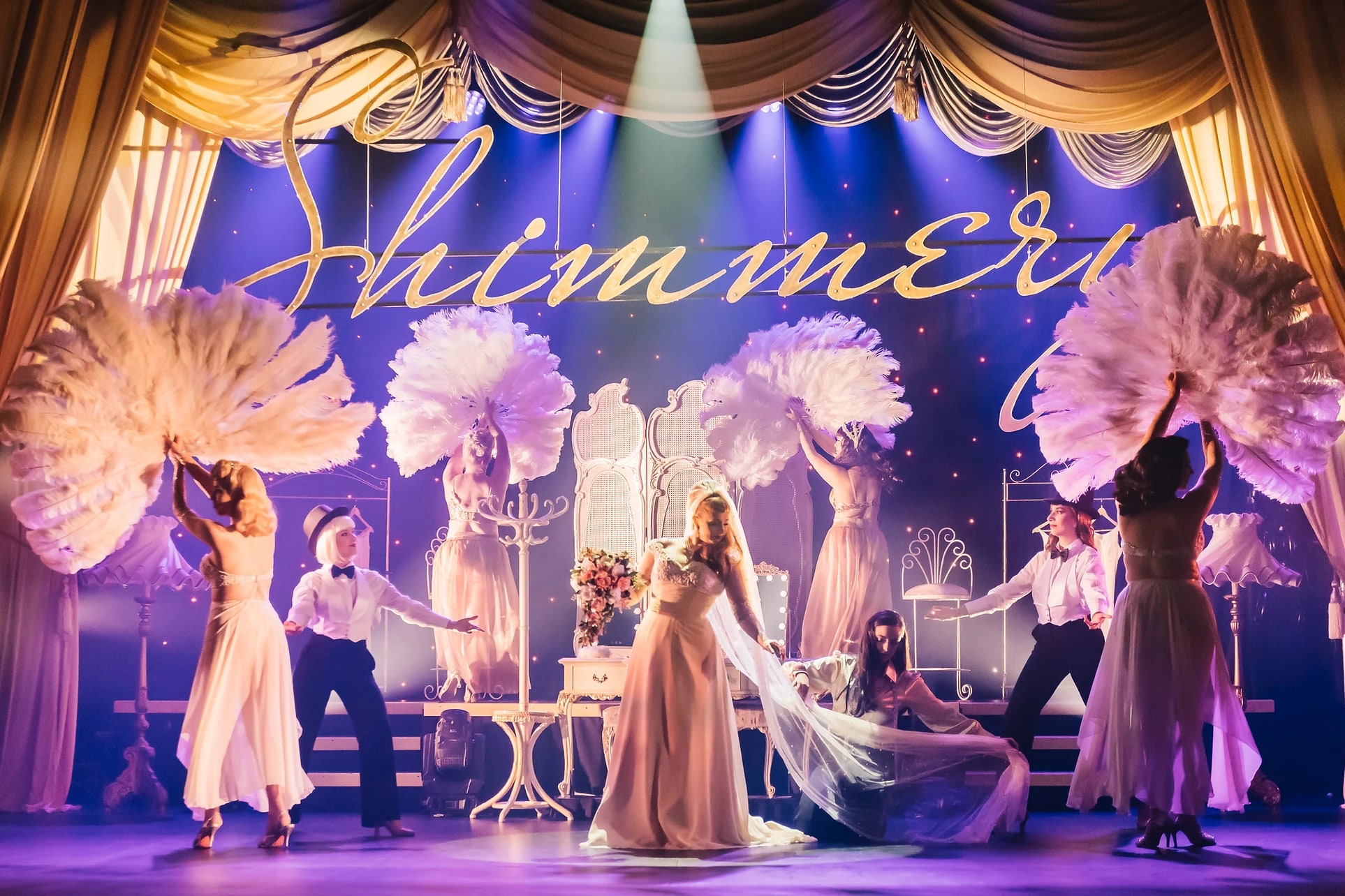 Showgirls with large white feather fans performing in front of the Shimmery sign