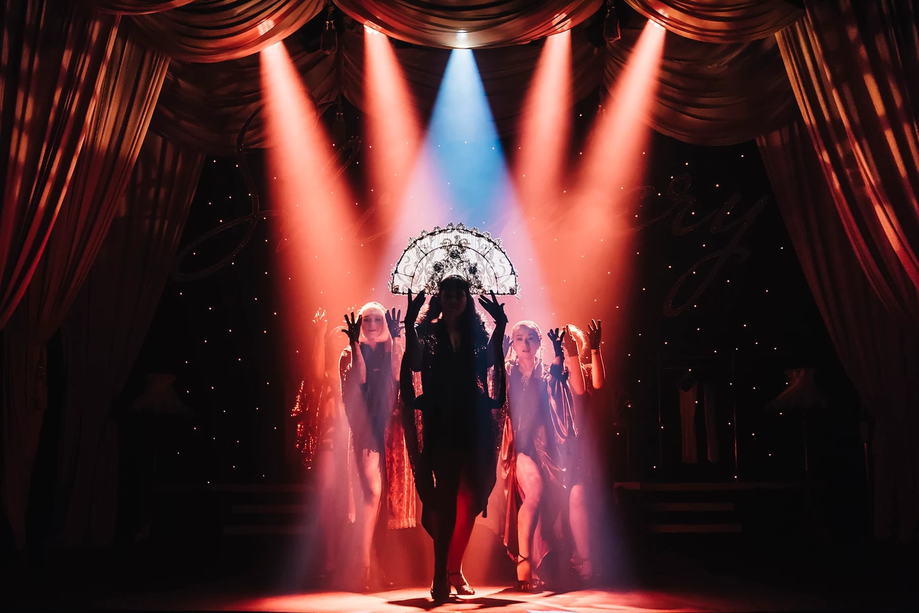 A performer silhouetted in pink and blue spotlights with a jewelled fan headpiece