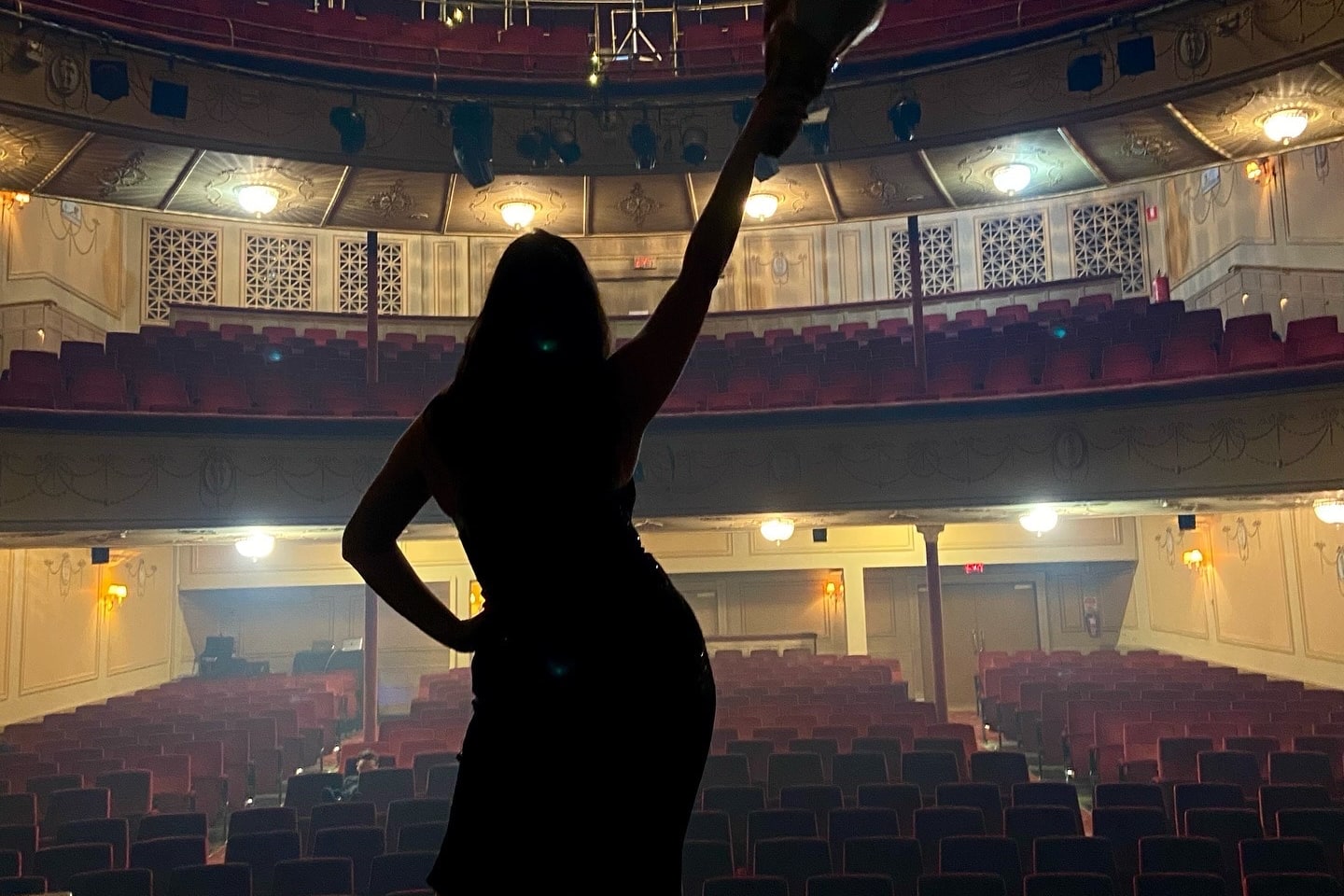 Abbey silhouetted on the Athenaeum Theatre stage with her arm raised towards the empty auditorium