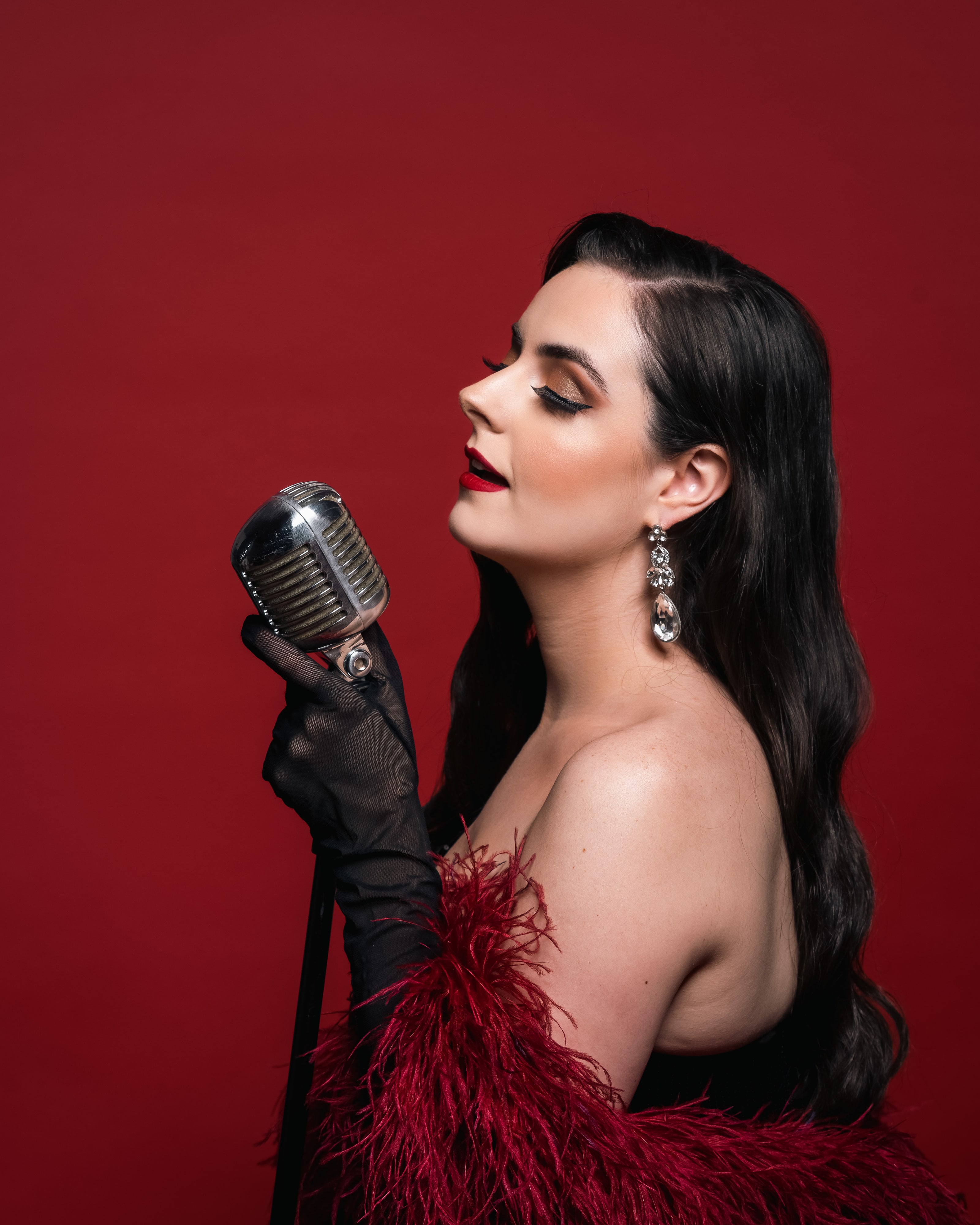 Abbey Williams side profile is seen holding onto her vintage microphone in front of a red background.