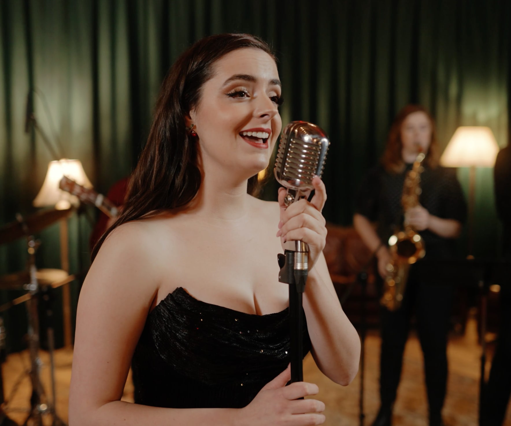 Abbey singing with her band in front of green velvet curtains