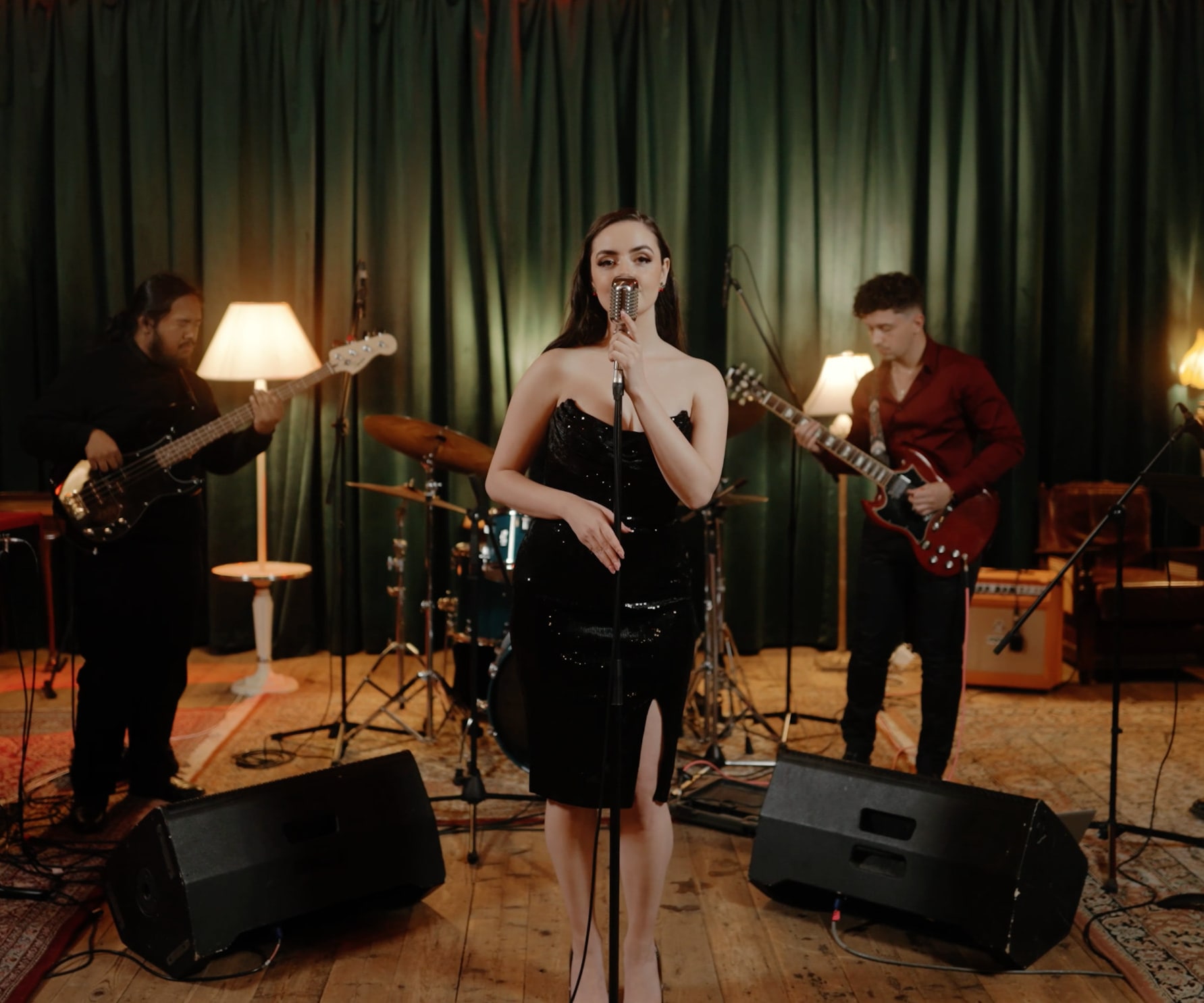 Abbey singing with her band in front of green velvet curtains