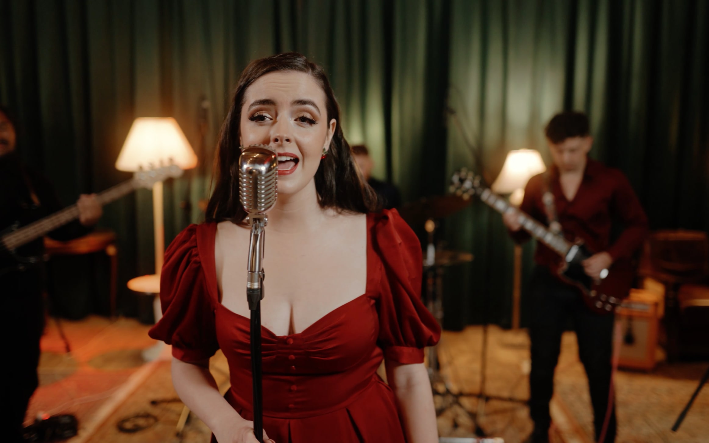 Abbey singing in a red puff-sleeved dress with the guitarist and bassist behind her