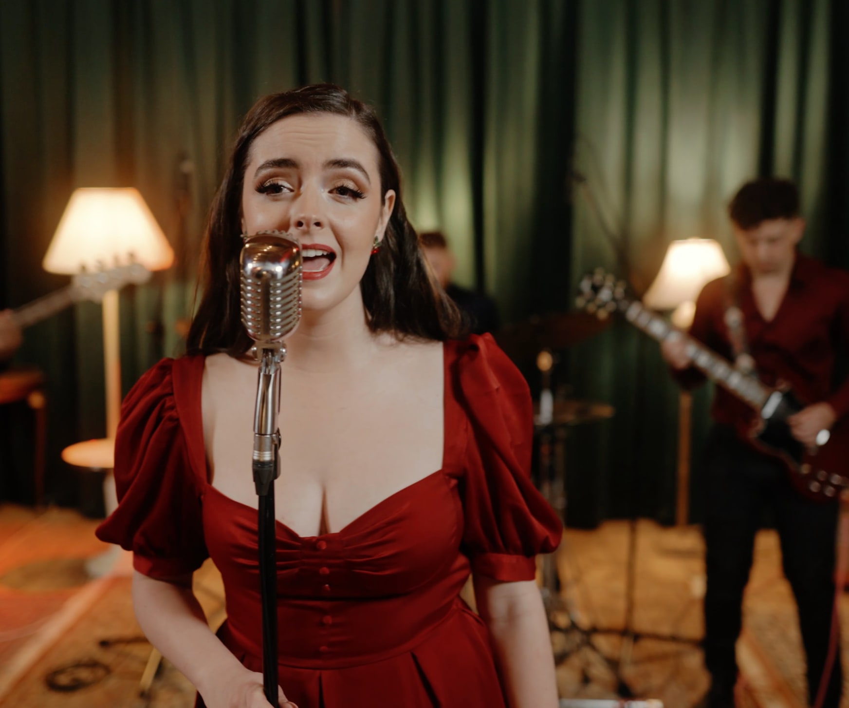Abbey singing with her band in front of green velvet curtains